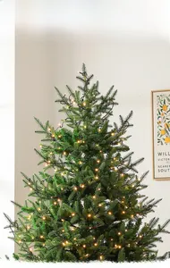 Primer plano de densas agujas verdes con luces LED amarillas cálidas en árbol de Navidad
