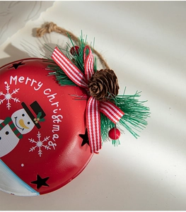 Macro view of a red metal Christmas bell with snowman pattern, pine cones and berries