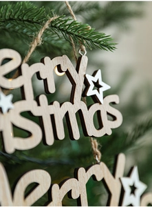Detail of wooden Merry Christmas hanging ornament with stars on a festive tree branch