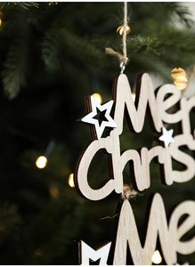 Detail of wooden Merry Christmas hanging ornament with laser-cut stars on a tree