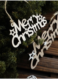 Close-up of a carved wooden Merry Christmas ornament hanging on a pine tree branch