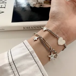 Detail of silver layered heart and star charm bracelets on a woman's wrist