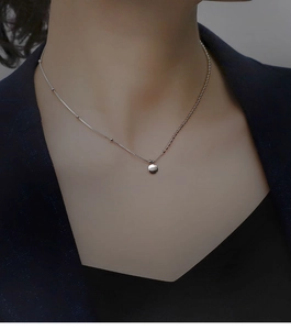 Close-up of asymmetric silver necklace with Lucky round pendant on dark suit background