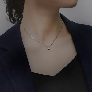 Close-up of silver lucky bean pendant necklace with lucky engraving on model