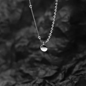 Detail of silver necklace with LUCKY pendant and asymmetrical bead and box chain design