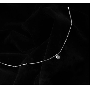 Detailed close-up of a silver bead necklace with a minimalist round engraved pendant
