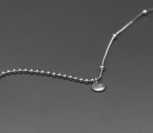 Macro shot of silver-tone split chain necklace featuring a round lucky engraved pendant