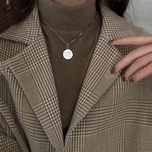 Detail of silver vintage necklace with engraved coin pendant on a brown sweater background