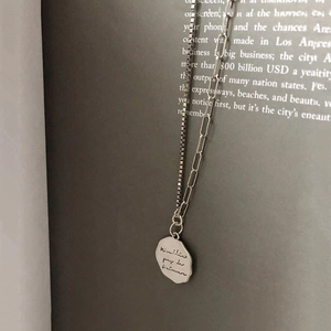 Close-up of asymmetric s925 silver necklace with engraved coin pendant on vintage book