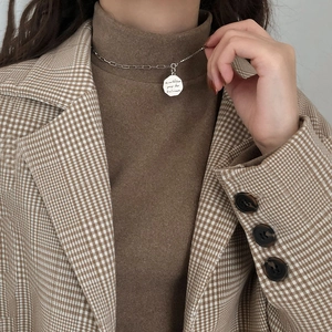 Close-up of a silver octagonal coin pendant necklace on a brown turtleneck sweater