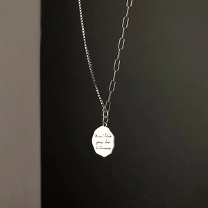 Detail of silver S925 necklace showing textured letter pendant and mixed chain link design