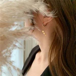 Detail of gold star tassel earrings on model featuring dainty chains and charms