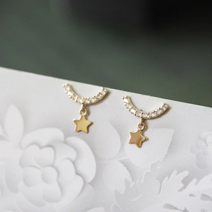 Macro detail of gold star stud earring with inlaid cubic zirconia on white card
