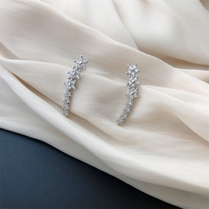 Detailed view of silver crawler earrings with sparkling star flowers on white silk background