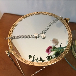 Detail eines Silberkettenarmbands mit Good Luck-Anhänger auf goldener Spiegelfläche