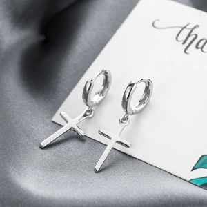 Macro detail of polished s925 silver cross pendant earrings on elegant silk background