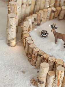 Close-up of flexible wooden branch fence on snow with warm LED lights and pine cones