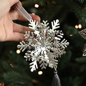 Silver metal snowflake ornament with crystal inlay and tassel on Christmas tree branch