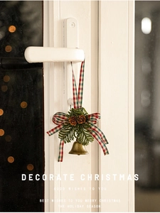 Detail of bronze metal bell with red plaid bow and pine cones on a door handle