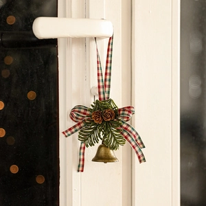Christmas bronze bell ornament with pine cones and tartan bow on white door handle