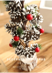 Close-up of rustic Christmas tabletop tree with snow-tipped pine cones and red berries