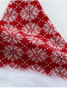 Detail of red knitted Christmas hat featuring white snowflake patterns and plush faux fur trim