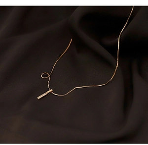 Dettaglio della collana con pendente a barra dorata e zirconi su raso marrone scuro