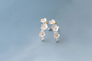 Macro shot of matte silver cherry blossom earrings with golden pistils on blue background
