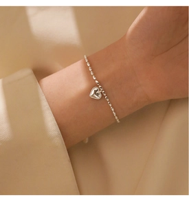 Close-up of minimalist S925 sterling silver rice bead bracelet with heart pendant on wrist