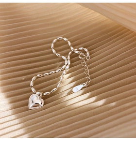 Macro detail of S925 sterling silver rice bead bracelet with heart charm on silk