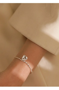 Detail of silver S925 heart pendant bracelet with polished rice beads on a model's wrist