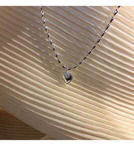 Close-up of S925 sterling silver heart pendant and beaded chain on beige fabric texture