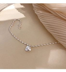 Detailed view of an S925 sterling silver heart charm and rice bead chain on a ceramic plate