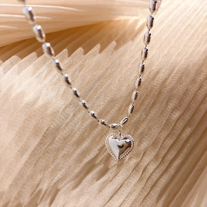 Polished silver heart pendant necklace with elegant rice bead chain on silk background