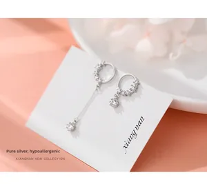 Detail of asymmetric S925 silver earrings with zircons on a white display card