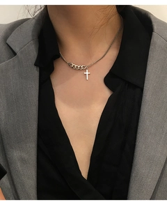 Close-up of asymmetric silver cross necklace worn on a black shirt and grey blazer