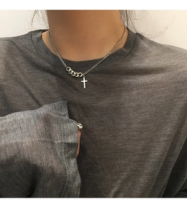 Detail of an asymmetrical silver cross necklace with thick and fine chains on a model