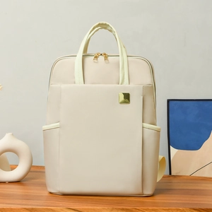 Gros plan du sac à dos beige avec plaque logo dorée sur fond en bois chaleureux