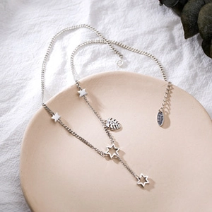 Detail of silver lucky star and monstera leaf charms on a minimalist dainty chain