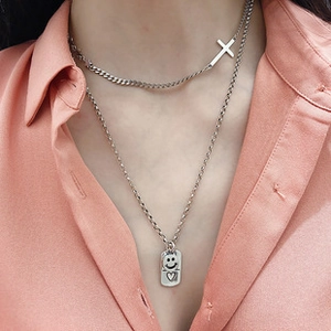 Close-up of layered S925 silver necklaces with cross and engraved smile face pendants