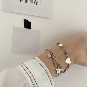 Dettaglio di braccialetti a strati in argento sterling S925 con ciondoli a stella e cuore al polso