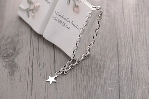 Detail of silver S925 star charm bracelet with lobster clasp on a white book prop