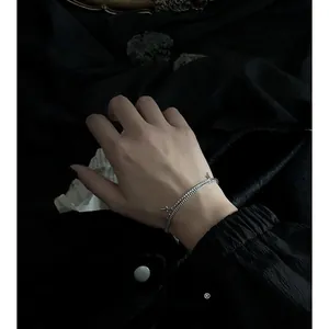 Dettaglio del bracciale a doppia catena d'argento con croce indossato al polso stile punk