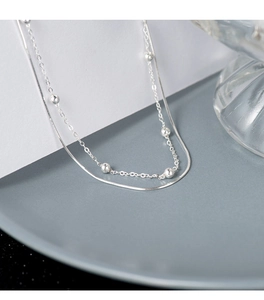 Detail of double-layer silver snake chain bracelet with smooth beads on a stylish tray