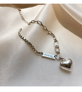 Gros plan d'un bracelet en argent S925 avec cœur et plaque Lucky Girl sur soie champagne