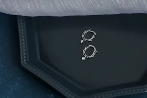 Macro detail of silver lace-edged earrings with round zircon drop on ceramic tray