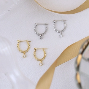 Close-up of U-shaped gold and silver earrings with lace edging and zircon pendants