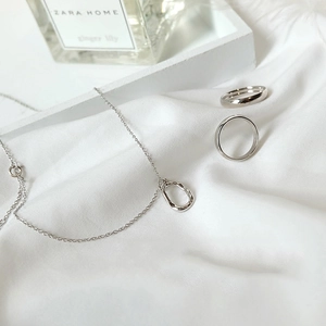 Minimalist S925 silver necklace with irregular oval pendant and simple rings set on fabric