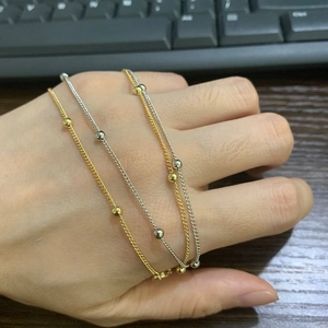 Gros plan de colliers minimalistes à perles dorées et argentées au design délicat sur la main