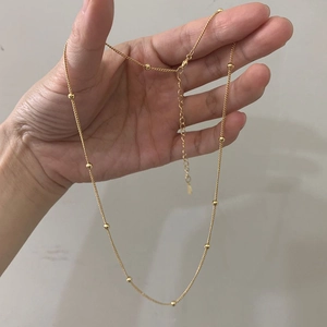 Détail d'un collier à billes dorées réglable avec fermoir mousqueton et extension